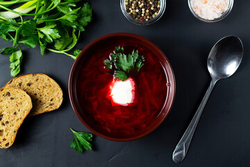 brown bowl of red beetroot soup with bread and herbs. borscht with sour cream, green parsley on the...