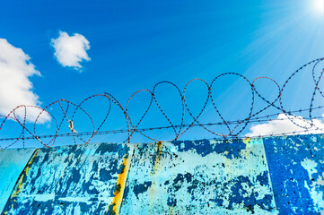 Fence in selective focus with barbed wire against freedom blue sky background.