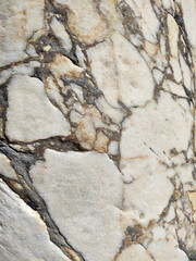 The texture of an old stone wall with pieces of white marble and gray pebbles, with cracks and veins