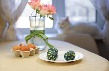 Easter eggs are painted on a white plate. green eggs with yellow spots. next to it is a vase of roses