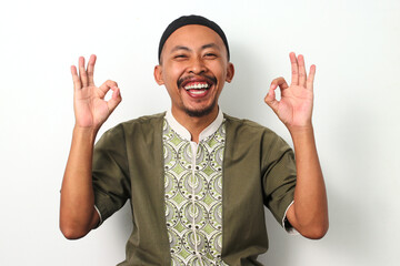 Happy Indonesian Muslim man in koko and peci shows an OK gesture, expressing satisfaction and...