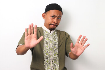 An Indonesian Muslim man in koko and peci holds up his palms in a gesture of refusal, demonstrating...