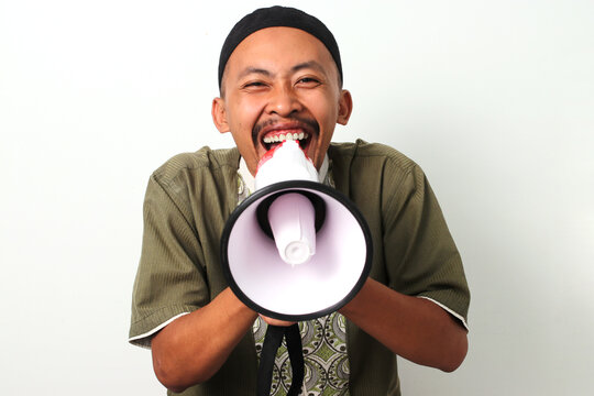 Excited Indonesian Muslim man in koko and peci shouts into a megaphone, announcing suhoor (pre-dawn meal) during Ramadan. Isolated on a White background