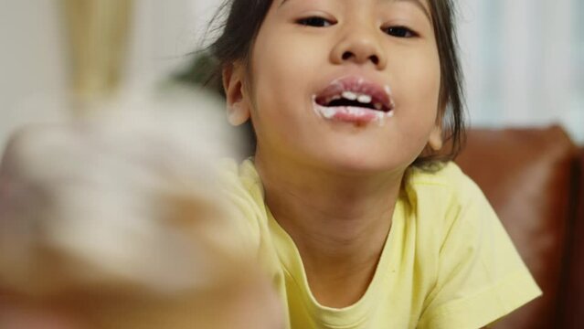 Footage handheld close up shot, Face of asian little girl eating ice cream until it was smeared, looking at camera Hand holding a ice cream forward to sharing