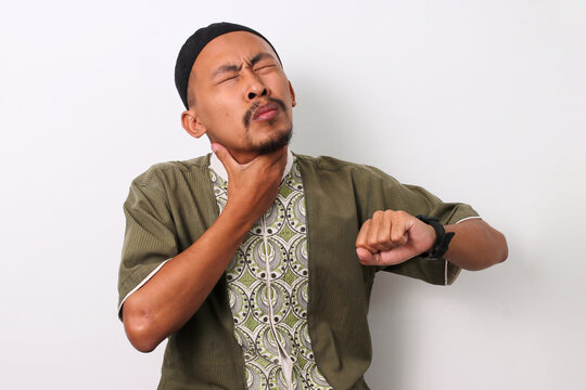 An Indonesian Muslim man holds his throat, feeling a sore throat while checking his watch. He's thirsty during the Ramadan fast, but it's not yet time to break fast. Isolated on a white background