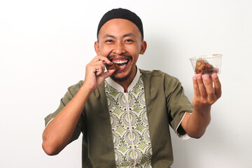Indonesian Muslim man in koko and peci eats a date during iftar, the sunset meal that breaks the...