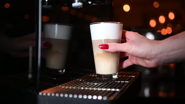 A woman's hand takes a glass with latte macchiato.