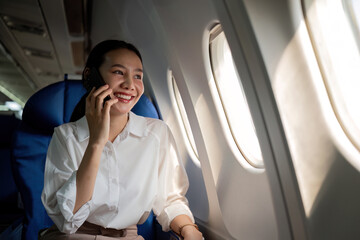 Smiling Asian woman enjoying a comfortable flight while sitting in an airplane cabin There is wireless internet on the plane. Passengers near the window