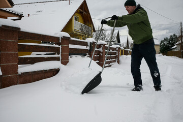 guy in jacket, hat and gloves shovels snow in front of house after blizzard - close up view