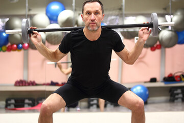 Middle aged man doing wide stance barbell squat in gym