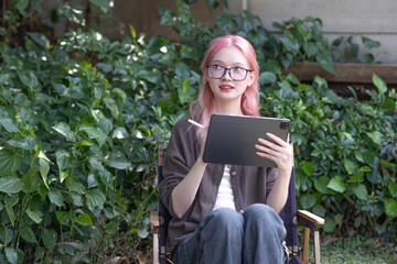 Cute and positive Asian woman recording data on a tablet or jotting down some ideas while sitting...