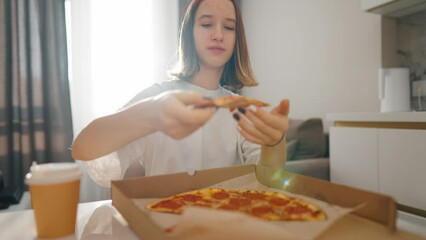 Close up little girl eating pizza food. Hungry happy young woman is eating piece of pizza, taking a bite from pizza indoor at home in a pizzeria. Fast food, children enjoying unhealthy food concept.