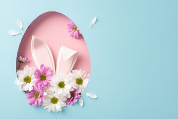 Joyful Easter creative scene. Top view photo showcasing amusing bunny ears popping out of an egg-shaped aperture, encircled by fresh chrysanthemums on a pastel blue backdrop, space for text