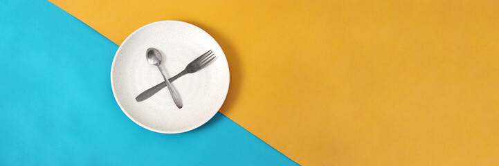 Empty plate with spoon and fork on a blue and yellow background with empty copy space for text or...