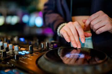 close-up of hands skillfully adjusting knobs and sliders on a professional DJ mixer, illuminated by colorful lights. The mood conveys focus and control during a live music event