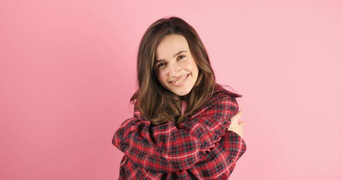 Come into my arms. Adorable happy girl with brown hair in plaid shirt gesturing come here for free hugs and smiling sincerely with welcoming expression isolated on pink background. Come to me!