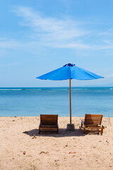 Sunbeds and a blue umbrella against the background of the sea. Concept of relaxing on the beach