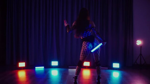 Sexy woman dancing twerk with flashlights in hands. Slow motion shooting. A dancer girl dances erotically in a dark hall. Twerk, high heels, striptease, a seductive dance. Atmospheric colored light