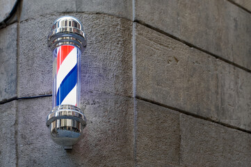A classic barber pole with illuminated red, white and blue stripes, mounted on a stone wall on a street in Barcelona in Catalonia Spain