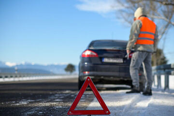 the driver of a motor vehicle had a car breakdown while driving on the road in the winter, he put a warning triangle on the road. close-up view and blurred background