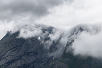 The mountain's rugged facade is veiled in a flowing mist, offering a textured contrast of solid and...