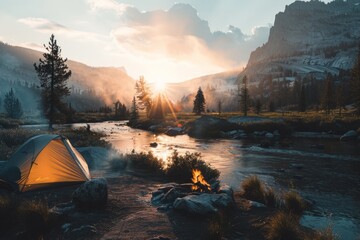 Camping tent set up by a river in a mountain valley with a campfire and the sun setting behind the peaks. - obrazy, fototapety, plakaty