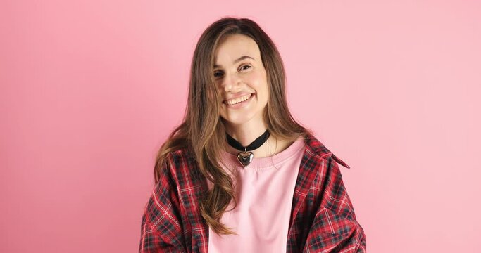 Smiling attractive brunette woman looking at camera listening to someone and nodding with agree standing over pink studio background. Girl wave her head, agree.