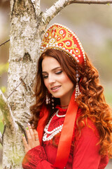 russian girl in traditional russian sarafan and kokoshnik embroidering outdoors