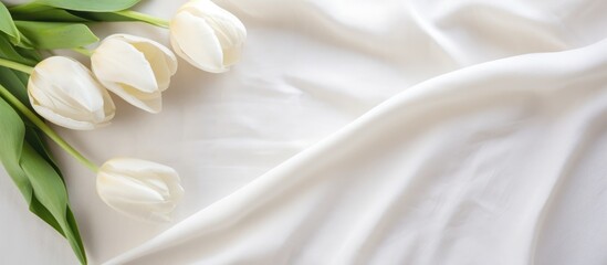 A bunch of white tulips is casually arranged on a white sheet. The delicate flowers contrast beautifully against the soft, natural fabric. The simple composition creates a clean and elegant aesthetic.