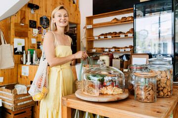Smiling woman buying organic food and eco products in sustainable plastic free store. Happy female customer shopping at local grocery shop.