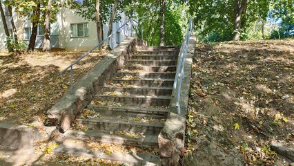 A concrete tile staircase with metal railings leads from a city park to a city block. Nearby are...