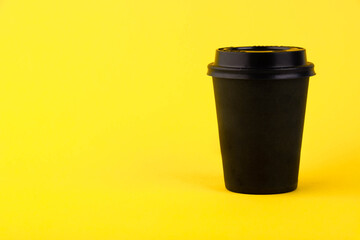 Eco black paper cup, coffee paper cup on yellow background. Mockup for your advertisement. Copy space.