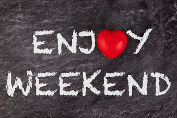 Enjoy weekend. The text is written on a school board with a white piece of chalk with a red heart. concept