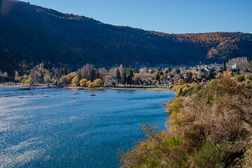 Fototapeta na wymiar Lakeside Town Panorama with Autumn Trees and Mountain Backdrop