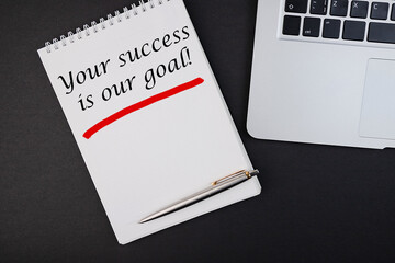 Your Success Is Our Goal notepad writing concept on dark background with pen.