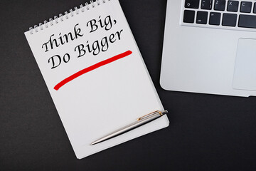 Think Big, Do Bigger Motivation quote notepad writing on dark background with pen.