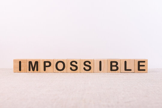 IMPOSSIBLE word concept written on wooden cubes lying on a light table and light background.