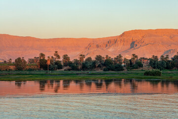 Landscape of mountains with palm trees on the Nile river banks, water reflections at sunset, Egypt - 748821531