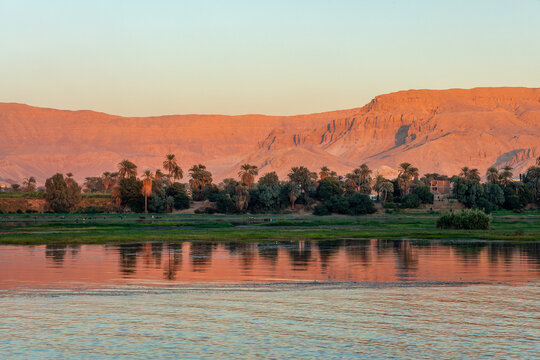 Landscape of mountains with palm trees on the Nile river banks, water reflections at sunset, Egypt