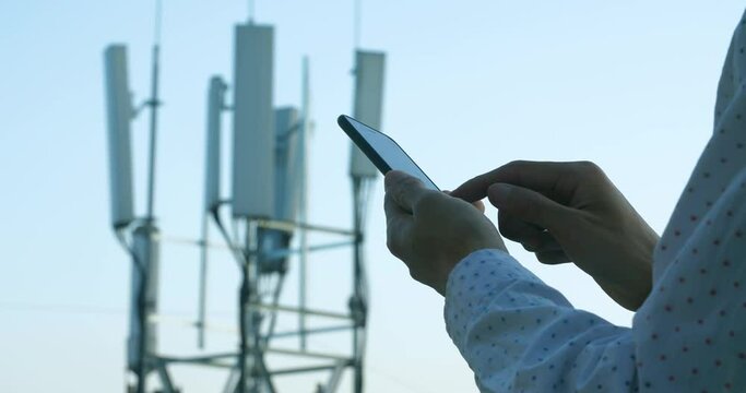 Men hand using phone with 5G Telecommunications base station tower background