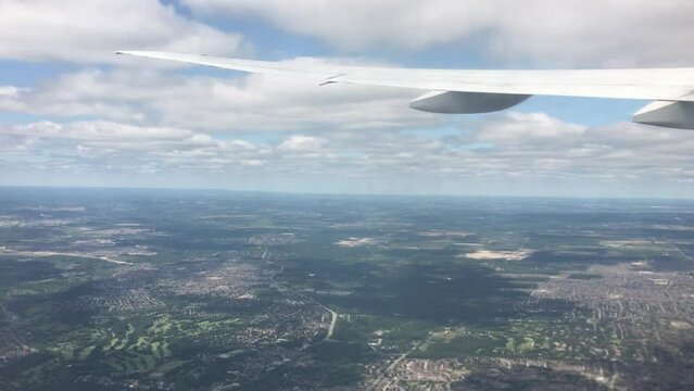 View out a commercial airliner window looking forward at the wing as it cuts through clouds as the plane climbs to altitude.