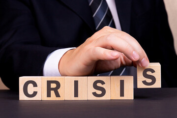 Obraz premium An American businessman is building the word Crisis from wooden building blocks. Business concept.