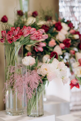 The wedding reception is decorated with glass vases, filled with white and pink tulips, surrounded by burning candles, which creates an intimate romantic atmosphere, close-up. Photo zone for a couple 