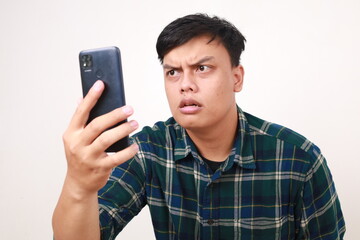 Close up photo of Confused expression of young asian man while holding a cell phone
