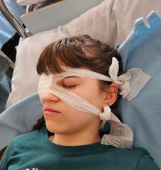 Obraz na płótnie Canvas A girl after surgery. Portrait of woman wearing white eye patch as protection after injury. Eye injury emergency first aid medical bandage of a young woman in the hospital