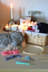 Balls of yarn, threads, various needlecraft needles and lit candles on the table. Hygge at home. Selective focus.