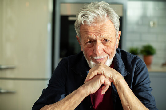 Portrait of a smiling elderly man with white hair and beard sitting indoors
