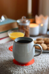 Cup of tea or coffee, stack of books, e-reader, glasses, various cookies, almonds, orange juice and lit candles on the table. Hygge at home. Selective focus.