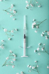 Cosmetology. Medical syringe and gypsophila flowers on turquoise background, flat lay