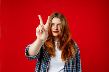 Cheerful 30s lady wearing checked shirt giving 2 sign isolated over bright red background, studio...
